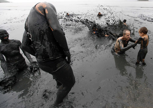 一位大人帮助小孩走入泥潭享受泥浴